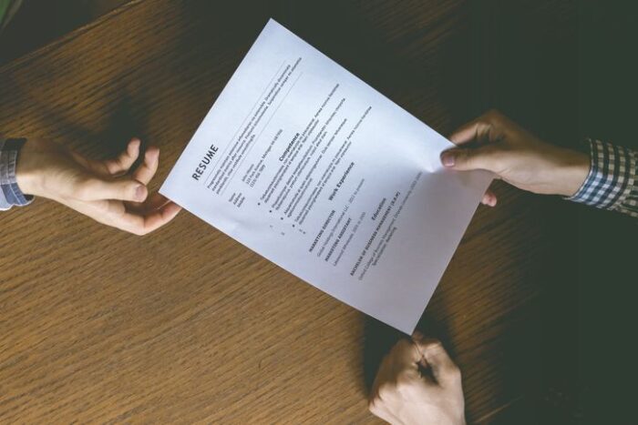 A resume being passed from one hand to another during a medical office specialist career job search.