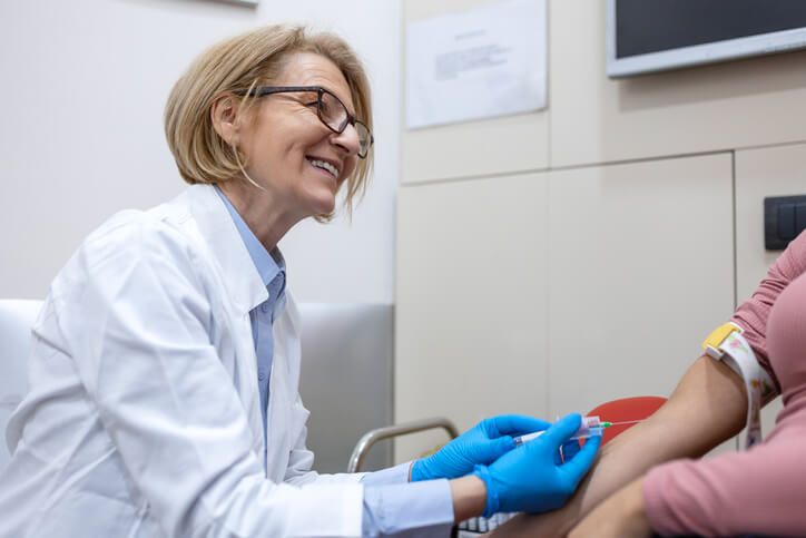 A smiling female phlebotomist preparing to draw a patient's blood after medical office specialist training