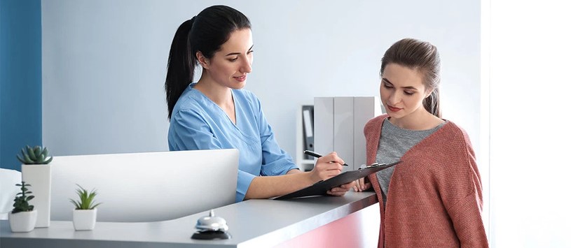 Medical Office Specialist speaking to a customer from behind a desk,